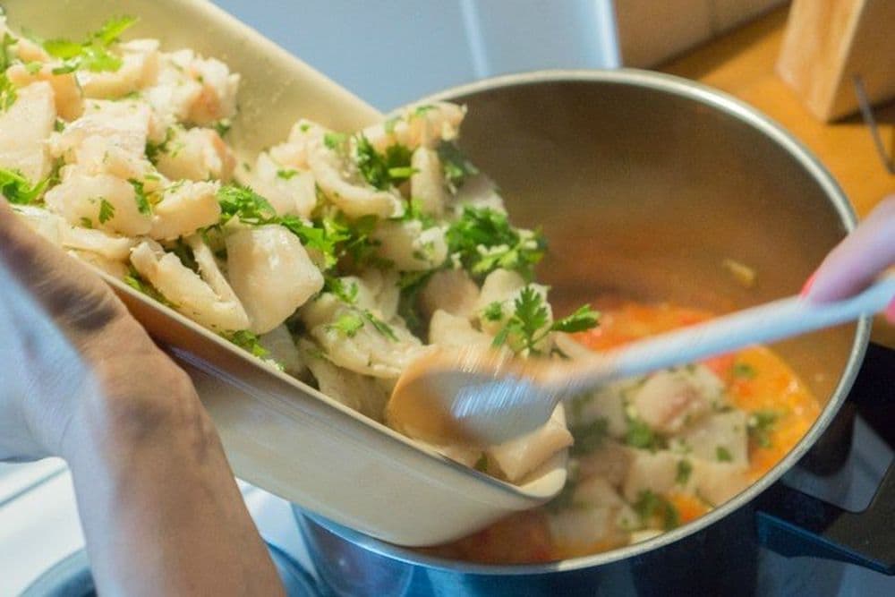 Fisch und Gambas werden in den Topf mit dem Gemüse geschüttet.